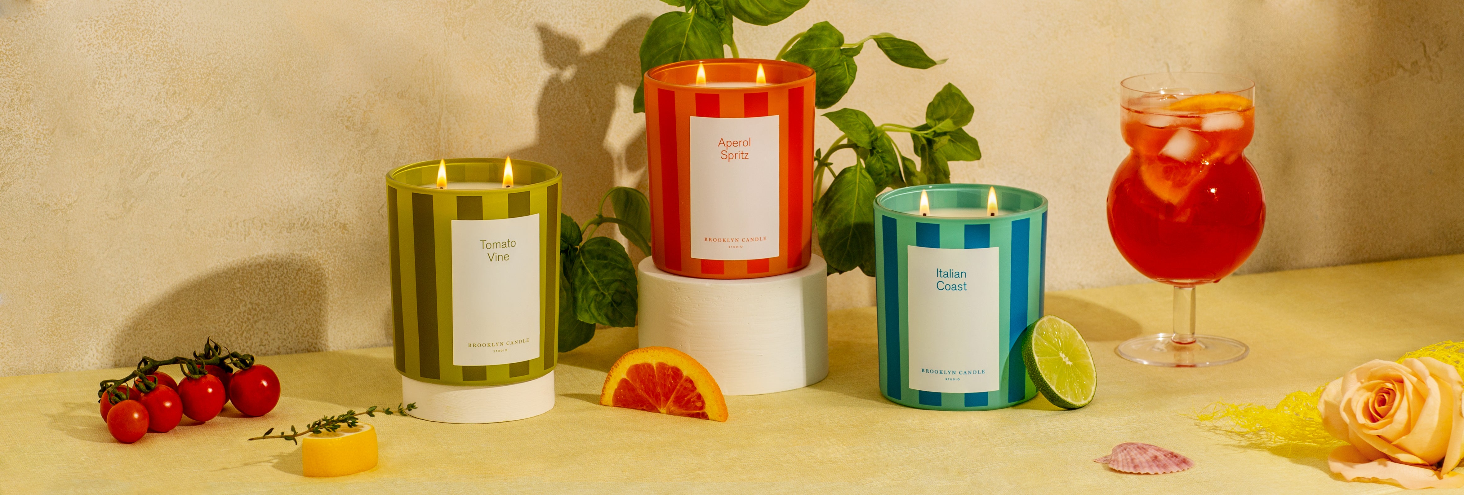 Tomato Vine, Aperol Spritz, and Italian Coast Candles on a table with fruits and a plant in the background